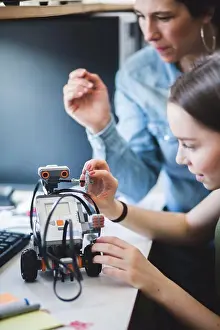 Innovation Prints: Female teacher assisting teenage student preparing robot on desk in classroom at high school