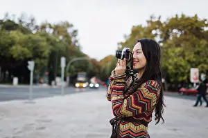 Hobbies Prints: Female tourist using camera on city street