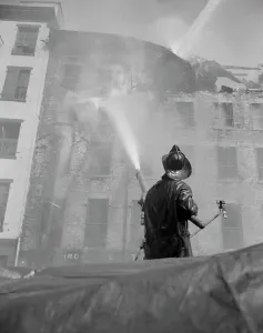 Firefighter Prints: Firefighter pouring water on burning building, low angle view
