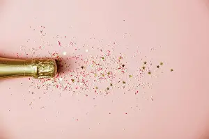 Pink Prints: Flat lay of Celebration. Champagne bottle with ice cream sprinkles and golden star sprinkles on pink background