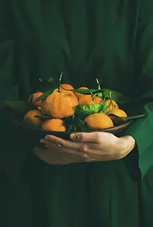 New Year Prints: Fresh raw tangerines citrus fruits with leaves in plate in hands of girl wearing green dress