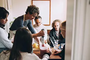Connexions Prints: Friends looking at teenage boy preparing smoothie at dining table in room