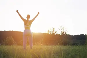 Dreaming Prints: a girl in a fitness suit stands with her back to the camera at sunset with her hands raised after