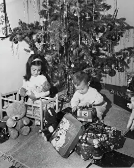 Curiosity Prints: Girl playing with a doll and her brother opening a Christmas present beside her, 1960s