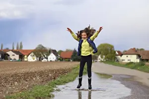 People In Nature Prints: A girl with raised arms jumps in a puddle