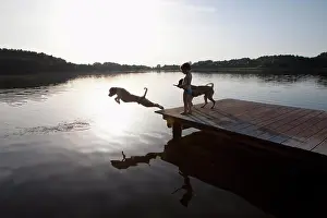 Child Hood Prints: Girl watching dog jumping off lakeside dock, Wiendorf, Mecklenburg-Vorpommern, Germany
