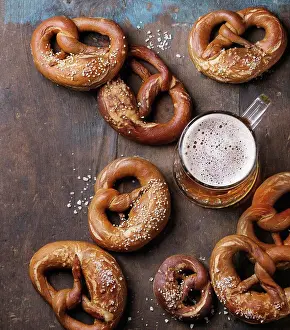 Beverage Prints: Glass of lager beer with traditional salted pretzels over old dark wooden background