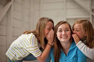 Conversation Prints: Grinning teenage girl listening while her two younger sisters whisper into both her ears