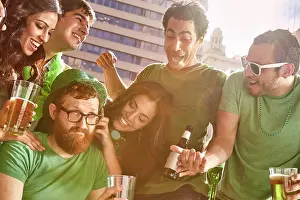 Multiracial Group Prints: Group of friends gathered around one man who is refusing to have fun at St Patrick's Day party