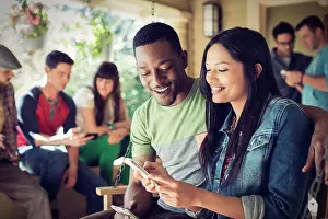 Midadult Men Prints: A group of friends, men and women at a house party, a woman holding a smart phone