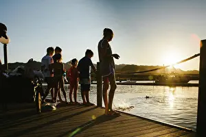 Large Group Prints: Group of kids stand on dock by lake in summer sunshine and feed fish