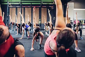 Athleticism Prints: Group of women training in gym with male trainer, bending forward with arm raised