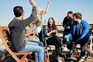 Coworker Prints: Group of young co-workers hanging out on rooftop patio having a drink and celebrating achievement reached on cell phone