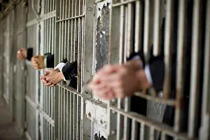 Doors Prints: Hands of a mid-adult business woman and three colleagues through bars of a prison cell in a derelict building