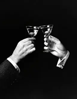 Two hands toasting with martini against black background