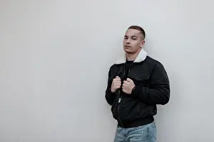 Stadt Prints: Handsome modernen jungen Mann in blauen stilvollen Jeans in trendigen schwarzen Jacke mit weißem Fell ruht in der Nähe