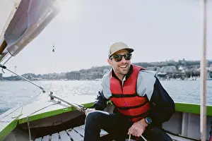 Life Jacket Prints: A handsome young man smiles and sails a small boat on a sunny day