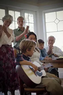 Grandma Prints: Happy family listening to a young boy playing a guitar at the dinner table