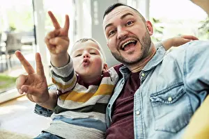 Upper Body Prints: Happy father and son gesturing peace sign in living room at home