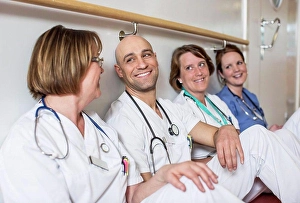 Mid Adultman Prints: Happy male doctor and female colleagues leaning together on wall in hospital