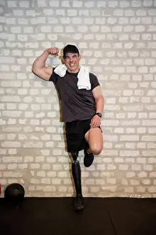 Handicapped Prints: Happy man with prosthetic leg flexing muscle near wall in gym