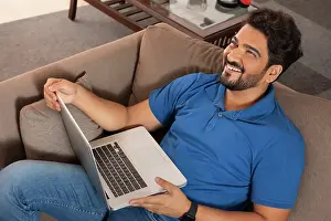 Home Office Prints: A happy man sitting on couch working on laptop at his home