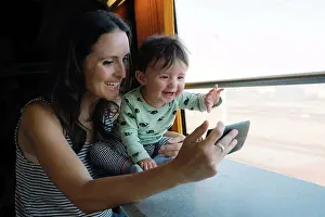 Curiosity Prints: Happy mother and baby girl using smartphone while traveling by train