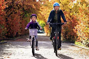 Equilibrium Prints: Happy mother and daughter cycling on road in park during autumn