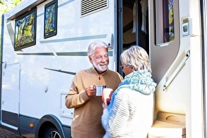 Grownups Prints: Happy senior couple holding coffee cup talking with woman by motor home