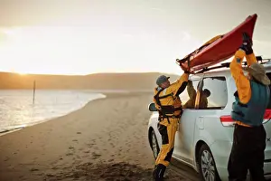 Out Door Prints: Happy senior couple lifting a sea kayak onto the roof of a SUV parked on a sandy beach