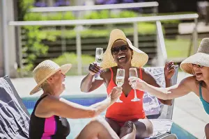 Baby Boomer Prints: Happy senior women friends drinking champagne at sunny summer poolside