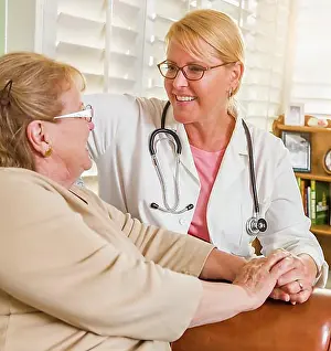Doctors Prints: Happy smiling doctor or nurse talking to senior woman in chair at home
