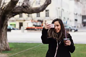 Disposable Prints: Happy woman photographing from smart phone while holding drink in city