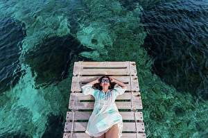 45 To 50 Years Prints: Happy woman wearing sunglasses lying on jetty amidst water