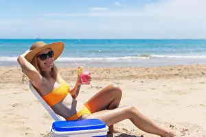 Straw Prints: Happy young european girl drinks a cocktail and rests in a sun lounger on the beach