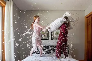 Gown Prints: Two happy young girls having a feather pillow fight on the bed