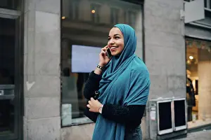 Using Phone Prints: Happy young Muslim woman talking on mobile phone walking building in city