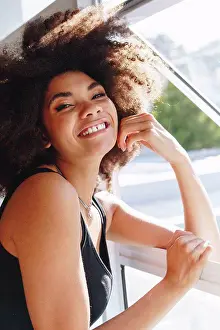Vest Prints: Happy young woman with afro hairstyle at bedroom window, head and shoulder portrait