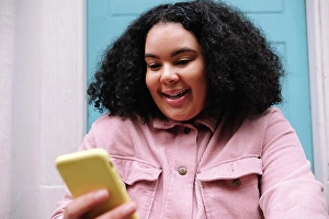 Top Section Prints: Happy young woman with curly hair surfing net through smart phone