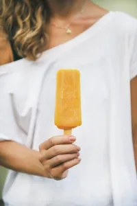 Mango Prints: Healthy vegan orange mango citrus ice cream popsicle in hand of young woman