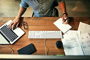 Organizing Prints: High angle shot of a businessman using a computer and writing notes during a late night at work