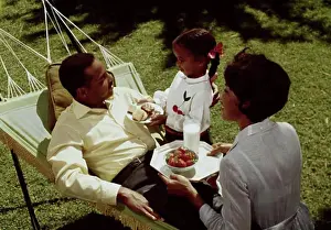 Lying On Back Prints: High angle view of a mid adult couple sitting in a hammock with their daughter standing beside them
