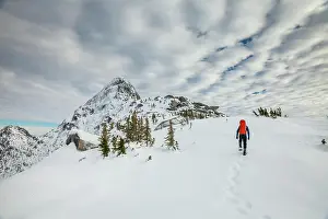 Tenacity Prints: Hiker approaches mountain summit wearing snowshoes, leaving footprints