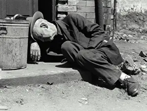 Poverty Prints: Homeless senior man sleeping near a garbage can