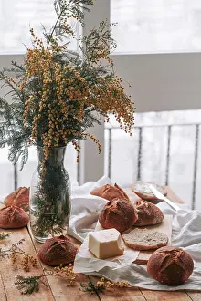 Composition Prints: From above of homemade round rye bread and butter on wooden table with vase of aromatic mimosa flowers in soft daylight