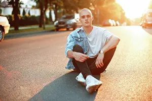 Stadt Prints: Hübscher junger Mann in modischer Jeanskleidung sitzt auf einer asphaltierten Straße bei Sonnenuntergang *** prettier