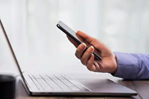 Innovation Prints: Human hand working on phone with a laptop in front
