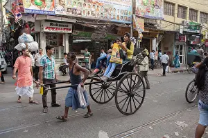India Prints: India, West Bengal, Kolkata, A rickshaw driver pulls passengers through the streets of the Bara Bazar district