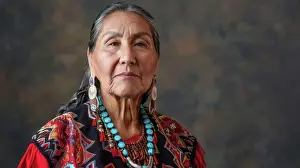 Elder Prints: An Indigenous elder woman with silver hair is wearing a beaded necklace