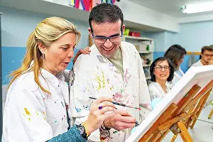 Disability Prints: Instructor helping a disabled man during painting class in a center for people with special needs